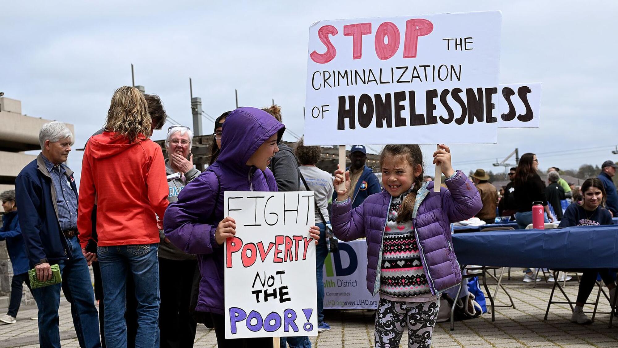 Two young children hold signs reading “Fight poverty not the poor” “Stop the Criminalization of Homelessness” 